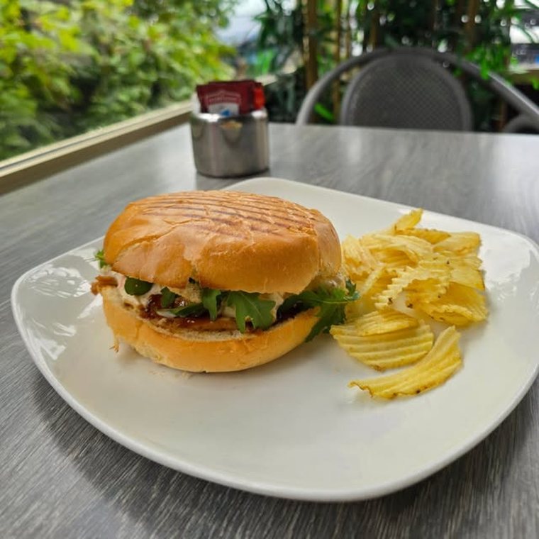 A filled bap with crisps on an outdoor table surrounded by greenery.