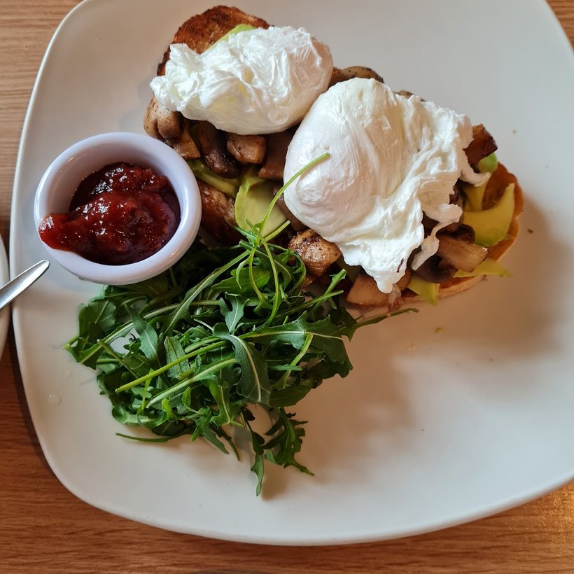 A brunch plate: poached egg, bacon and mushrooms on sourdough with rocket and a pot of relish.