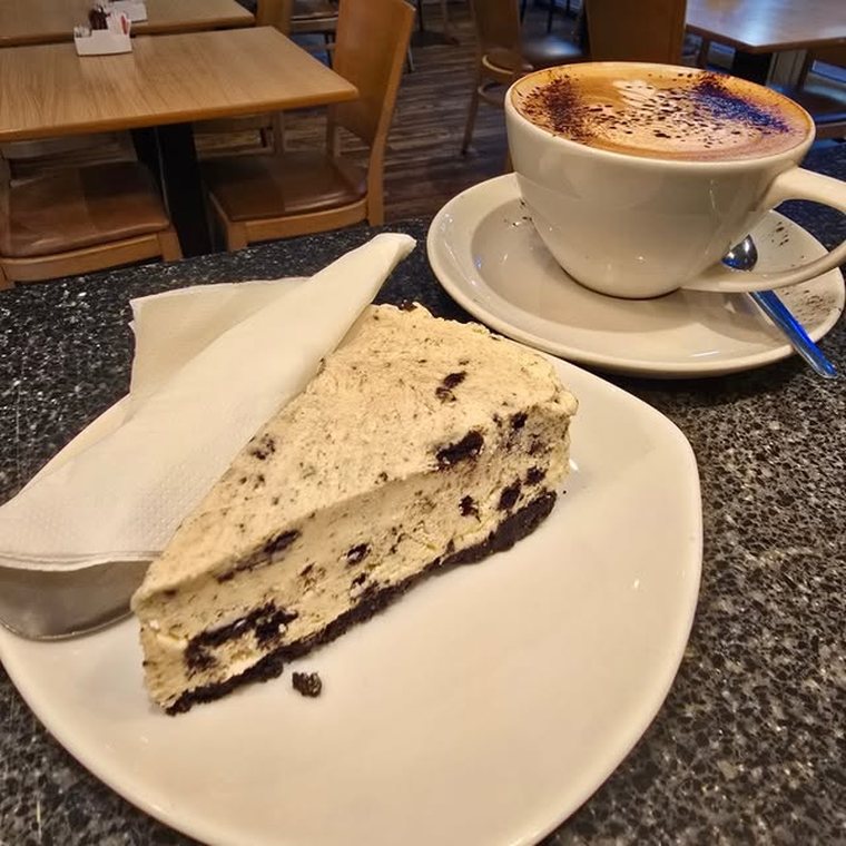 A slice of cookie cheesecake beside a cappuccino.