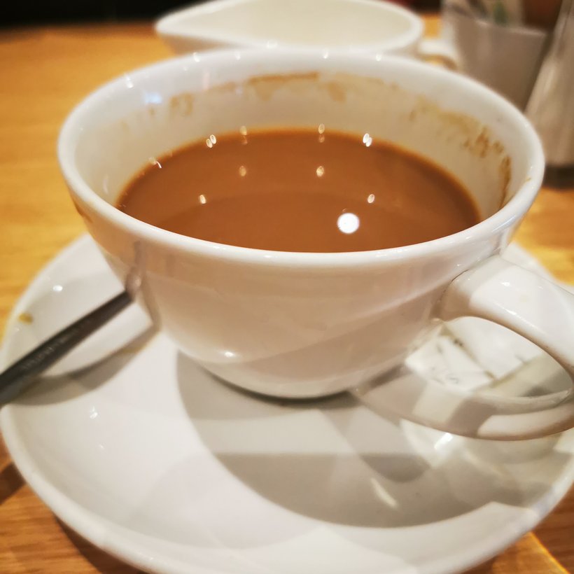 A cup of coffee on a saucer on one of the wooden tables.