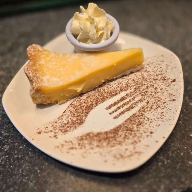A slice of tart with cream, on a plate decorated with a cocoa-dusted fork print.