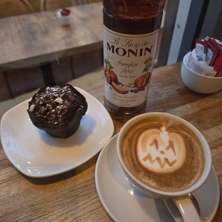 A latte with a pumpkin face poured into the foam, beside a chocolate muffin.