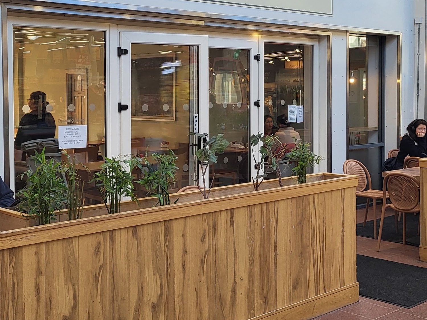 The entrance to Cates Café: glazed double doors with the opening hours posted beside them, and bamboo planters along the front.
